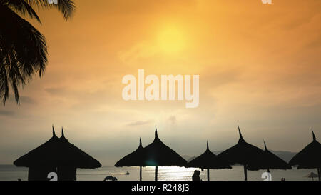 Sagome di sedie da spiaggia in cielo di sera in Vietnam con palme. Vista di ombrelloni da un torrente sulla spiaggia durante il tramonto. Foto Stock