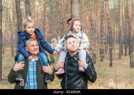 Ritratto di una figlia e la nipote sulle spalle di papà e nonni in una foresta di conifere Foto Stock