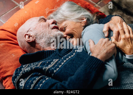 Felice coppia senior di dormire sul pavimento che abbraccia ogni altra in una fredda notte. Senior sorridente donna che dorme tra le braccia di suo marito felicemente. Foto Stock