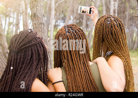 Tre giovani e belle ragazze, con capelli intrecciati, tenendo selfie Foto Stock