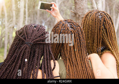 Tre giovani e belle ragazze, con capelli intrecciati, tenendo selfie Foto Stock