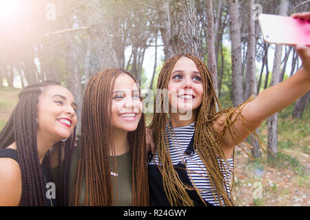 Tre giovani e belle ragazze, con capelli intrecciati, tenendo selfie Foto Stock