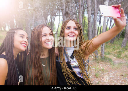 Tre giovani e belle ragazze, con capelli intrecciati, tenendo selfie Foto Stock