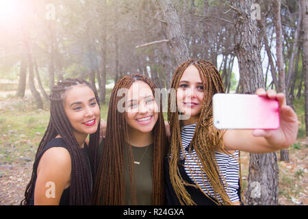 Tre giovani e belle ragazze, con capelli intrecciati, tenendo selfie Foto Stock