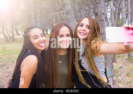 Tre giovani e belle ragazze, con capelli intrecciati, tenendo selfie Foto Stock