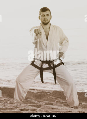 Giovane uomo a praticare il karate le posizioni a ocean quay in sunset Foto Stock