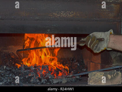 Il fabbro suscita e stokes le fiamme dentro il buio e grungy fucina di carbone Foto Stock