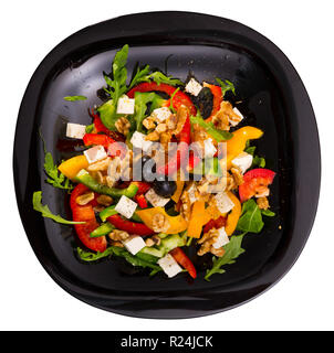 Vista superiore della vitamina insalata di rucola con peperoni e formaggio feta decorate con olive e noci servita nella piastra nera su striped backgro tessili Foto Stock