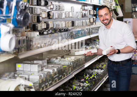 Sorridente uomo adulto selezionando presa elettrica nel dipartimento di uso domestico Foto Stock