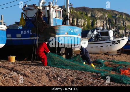 Barche di pesca, lo stade, storica spiaggia di pesca. Un pescatore raccoglie le sue reti da pesca di fronte alle barche da pesca sulla sola spiaggia ha lanciato la flotta di pesca nel regno unito dopo una mattina fuori in mare. Hastings, East Sussex, regno unito Foto Stock