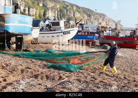 Barche di pesca, lo stade, storica spiaggia di pesca. Un pescatore raccoglie le sue reti da pesca di fronte alle barche da pesca sulla sola spiaggia ha lanciato la flotta di pesca nel regno unito dopo una mattina fuori in mare. Hastings, East Sussex, regno unito Foto Stock