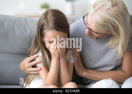 Amorevole comprensione nonna abbracciando poco ragazza che piange comfor Foto Stock