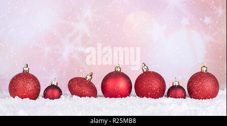 Rosso baubles di Natale sulla superficie nevosa e caduta di neve su un brillante sfondo per le vacanze Foto Stock