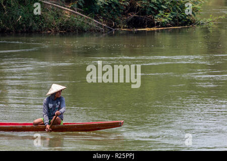 Don Det, Laos - Aprile 24, 2018: Locale boy canottaggio un rosso in legno barca lunga attraverso il fiume Mekong Foto Stock