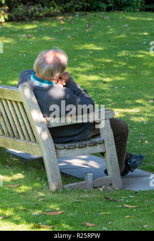 Anziani o uomo più anziano di dormire su una panchina nel parco in autunno. l uomo dorme e relax su una tavola di legno una panchina nel parco. Foto Stock