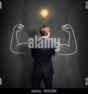 Imprenditore di successo in piedi di fronte a una lavagna con un brillante lampadina sopra la sua testa Foto Stock