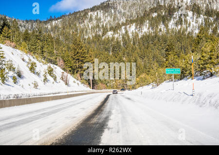 La guida su ghiaccio e neve coperto la strada attraverso le montagne di Sierra in una giornata di sole; Carson City cartello stradale sulla destra; Nevada Foto Stock