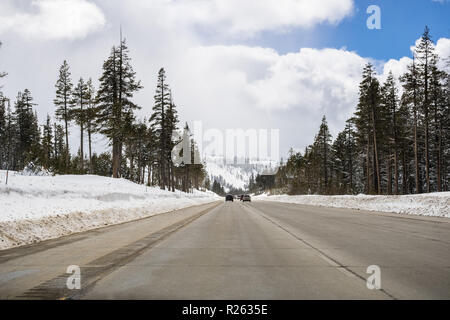 Vetture guida su I80 interstate attraverso la Sierra Mountains vicino al lago Tahoe su una soleggiata giornata invernale; la strada è stato cancellato sulla neve, California Foto Stock