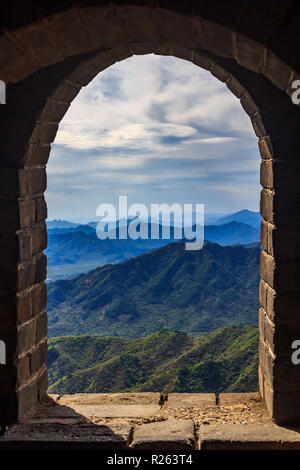 Vista su una catena montuosa attraverso una finestra in una delle torri di avvistamento della Grande Muraglia cinese, nel villaggio di Mutianyu, nei pressi di Pechino Foto Stock