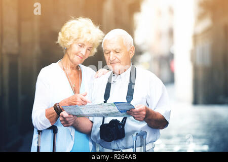 Sorridenti coppia senior di turisti con mappa e guida della città a piedi su strada Foto Stock