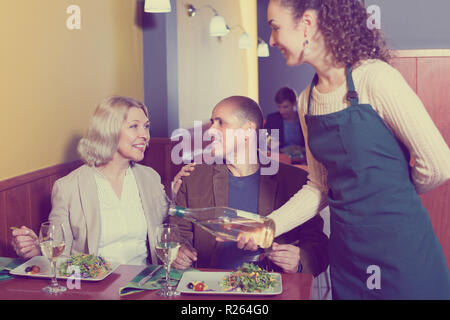 Cameriera serve positivo ospiti senior giovane al tavolo nel ristorante Foto Stock