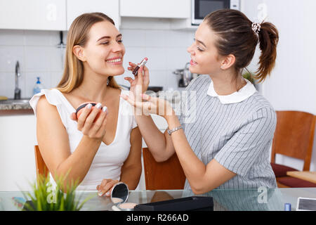 Due ragazze moderne amici parlando e applicare il make up in cucina Foto Stock