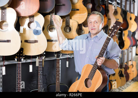 Musicista acquirente è in piedi accanto a chitarre acustiche nel negozio di musica. Foto Stock