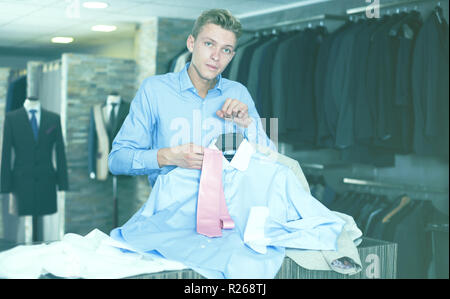 Acquirente maschio in camicia scegliendo cravatta e camicia nel negozio di abbigliamento Foto Stock