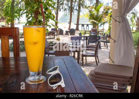 Arancione o succo di mango accanto a occhiali da sole in piedi sulla tavola in bar sulla spiaggia Foto Stock