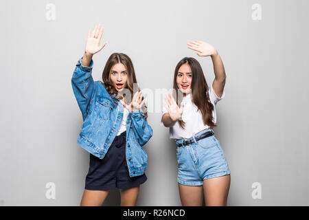 Due giovane e bella ragazza su uno sfondo grigio con facce gravi e il gesto delle mani Foto Stock