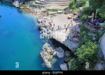 Agosto 2013, Mostar. Turisti e spettatori realaxing sulla banca del fiume Neretva in attesa del prossimo ponte/ponticello subacqueo. Foto Stock