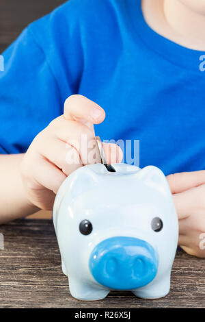 Una banca di colore blu per le monete in cui un bambino si ripiega e salva i suoi risparmi, pocket money, un suino a forma di salvadanaio Foto Stock