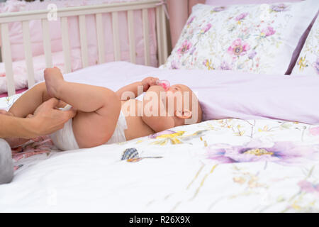 Le madri mano controllando il suo pannolino per bambino, mentre lei pone sul retro su lenzuola sul letto, visto in close-up con spazio di copia Foto Stock