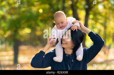 Amorevole Madre dando la sua bambina un giro sulle sue spalle come trascorrere una giornata felice in un colorato parco di autunno Foto Stock