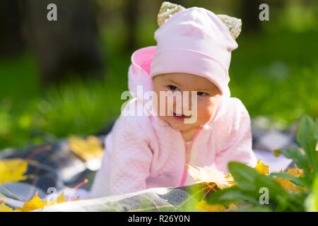 Piuttosto allegro little Baby girl in un autunno park strisciare su di essa una coperta sull'erba verso la telecamera con un sorriso Foto Stock