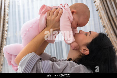 Amorevole Madre a giocare con la sua piccola bambina il suo sollevamento in alto in una chiusura gara ritratto al coperto Foto Stock