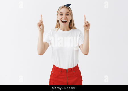 Non è in grado di fermare la gustano la vita. Ritratto di affascinante bionda spensierata donna in abiti eleganti, solleva le dita indice al punto fino, sorridente largamente e ridere Foto Stock