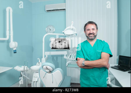 Sorridente maschio caucasico medico guardando la fotocamera in studio dentista, panoramica x-ray sullo schermo, una persona, modello rilasciato Foto Stock