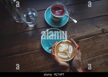 Mani femminili in possesso di una tazza di caffè un dessert su un tavolo di legno Foto Stock