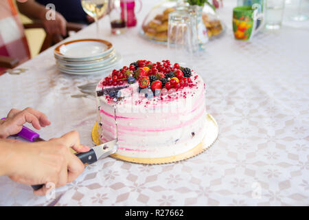 La mano con il coltello per affettare la torta di compleanno Foto Stock