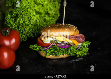 Gustosa cheesburger con un gran numero di verdure, senape, maionese, salame e viola per anelli di cipolla Foto Stock