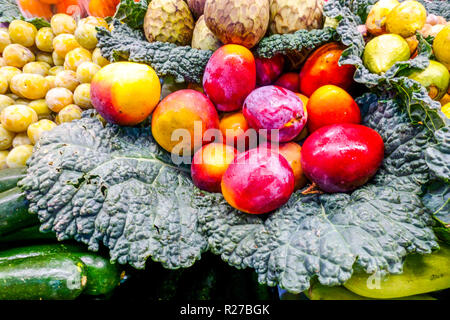 Mango rosso fresco e prugne gialle sistemate sulle foglie di cavolo della savoia in un mercato agricolo di Valencia, Spagna. Foto Stock