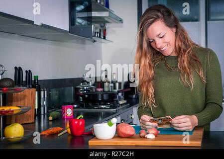 Giovane donna sorridente leggendo la ricetta di cucina con ingredienti freschi. Concetto di ringraziamento. Foto Stock