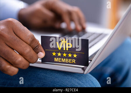 Close-up di una mano di un uomo azienda VIP Member Card durante l'utilizzo di Laptop Foto Stock