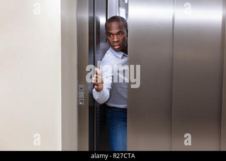 Giovane africano cercando di smettere di ascensore porta con la sua mano Foto Stock