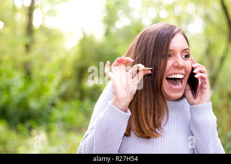 Bruna giovane ragazza ridere molto espressiva con il denaro in mano a parlare al telefono perché lei ha vinto la lotteria Foto Stock