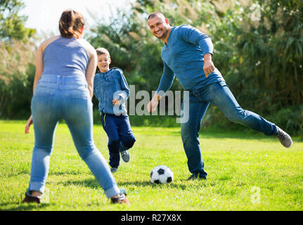 Ritratto di active famiglia allegra che giocano a calcio con figlio all'aperto Foto Stock