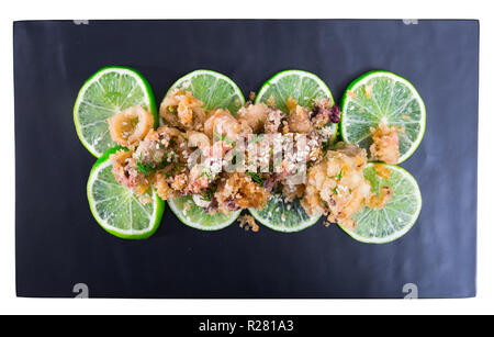 Vista dall'alto di calamari e seppie in tempura con spicchi di lime sottaceto su nero che serve board. Isolato su sfondo bianco Foto Stock