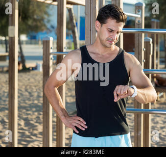 Montare fisicamente un uomo guarda smartwatch sulla terra di sport sulla spiaggia Foto Stock