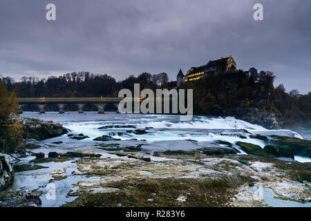 Paesaggio verticale vista sulle famose cascate del Reno in Svizzera la sera durante il tramonto con un treno sfocata attraversando il ponte Foto Stock